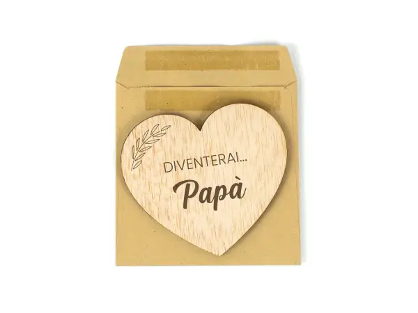 Cuore di legno con scritta "Diventerai... Papà", un dolce annuncio di gravidanza in una busta marrone.
