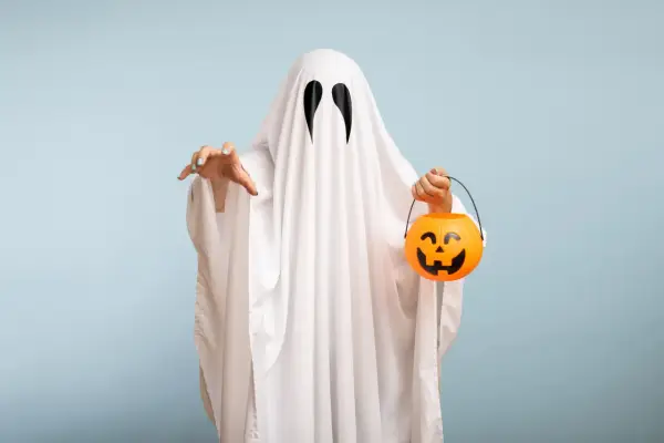 Bambino con costume da fantasma fai da te, tiene un cestino di caramelle a forma di zucca.